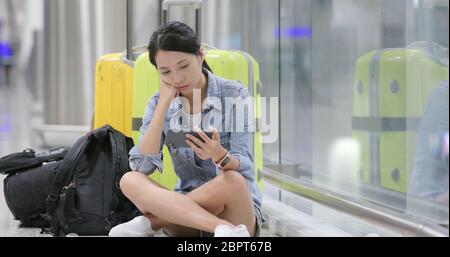 Une femme joue au jeu sur son téléphone portable et attend son vol à l'aéroport avec ses bagages et son sac à dos Banque D'Images