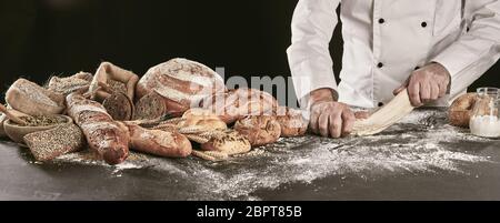 Baker le pétrissage pâte crue tout en faisant un assortiment de pains spéciaux affichés à côté sur une surface enfarinée dans panorama format bannière compteur Banque D'Images