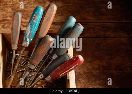 Manches en bois de vieux millésime tournevis calé debout dans une caisse en bois avec des vis dans le bas sur une table ou un établi rustique vue h Banque D'Images