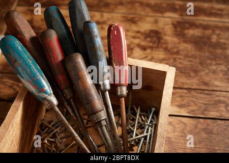 Jeu de tournevis old vintage usé avec poignées en bois debout dans une caisse en bois avec différents équipages dans le bas sur une table rustique Banque D'Images