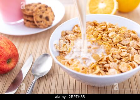 Petit déjeuner verser du lait dans des flocons de maïs créant des biscuits aux pommes et aux fruits orange Banque D'Images