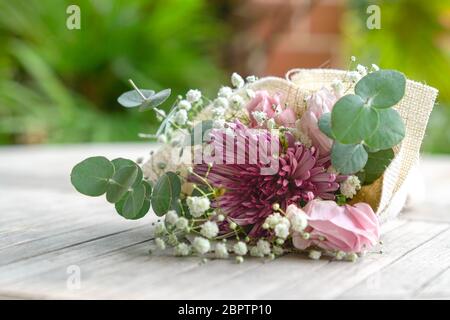 Le bouquet de fleurs à la main se compose de chrysanthème, de roses et de feuilles vertes. Sur la table. Banque D'Images