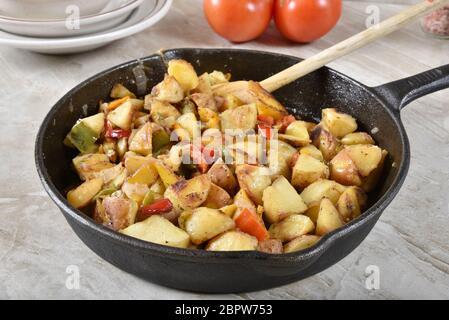 Quartiers de pommes de terre rôtis avec oignon, ail, poivron vert et rouge dans une poêle en fonte Banque D'Images