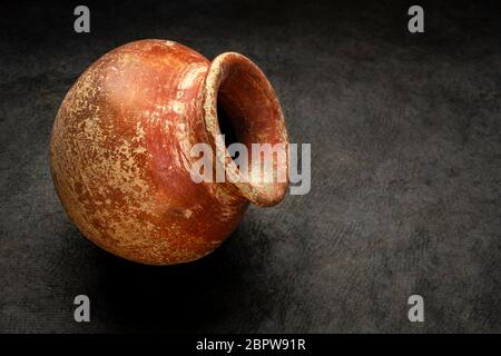 petite casserole en argile rouge et brune (semoir produit en masse) avec finition rugueuse, grince sur fond de papier texturé foncé Banque D'Images