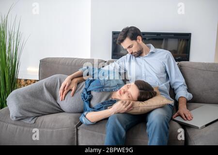 Jeune femme enceinte dans une veste de Jean qui pose sur les longueurs de son mari Banque D'Images