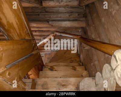 Un escalier avec une descente en spirale, des marches en bois pliées, recouvert d'un vernis brun foncé d'un design traditionnel dans une maison avec une maison en rondins. Banque D'Images