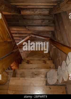 Un escalier avec une descente en spirale, des marches en bois pliées, recouvert d'un vernis brun foncé d'un design traditionnel dans une maison avec une maison en rondins. Banque D'Images