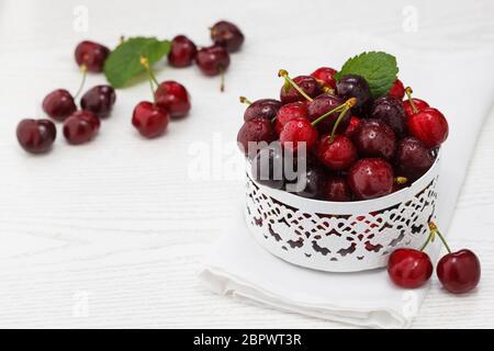 Bol de cerises douces fraîches avec feuilles dans des gouttes d'eau sur une table en bois blanc. Banque D'Images