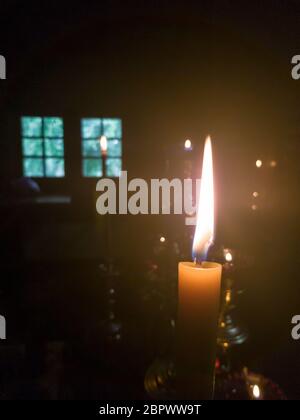 Une bougie jaune avec une longue flamme dans l'autel d'une église orthodoxe près du trône avec une menorah face à la fenêtre au crépuscule Banque D'Images