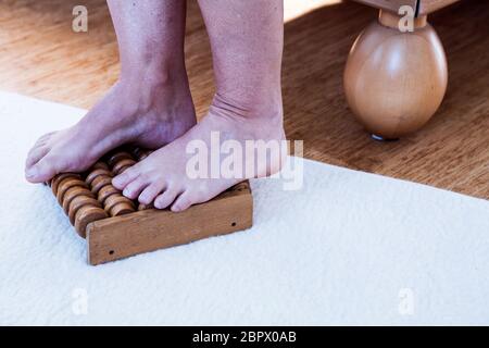 gros plan des pieds sur un rouleau de massage en bois sur un tapis blanc Banque D'Images