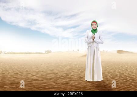 Smiling Asian Muslim woman in veil priant sur la dune de sable avec fond de ciel bleu Banque D'Images