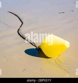 Une grande bouée jaune et sa chaîne d'ancrage, utilisée comme marqueur de canal de lancement, se trouvant sur le sable humide à marée basse sur la plage au soleil. Banque D'Images