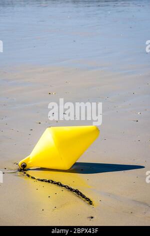 Une grande bouée jaune et sa chaîne d'ancrage, utilisée comme marqueur de canal de lancement, se trouvant sur le sable humide à marée basse sur la plage au soleil. Banque D'Images