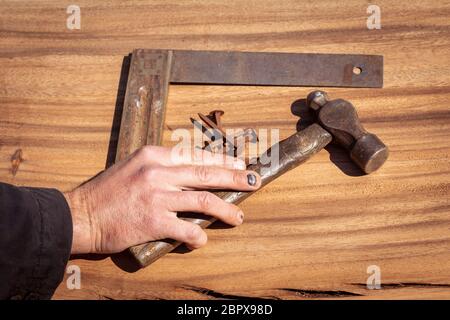 Main d'un charpentier avec des ongles noirs meurtrisés ramassant un vieux marteau d'époque d'une dalle en bois. Accident de travail avec traumatisme sur les doigts cau Banque D'Images