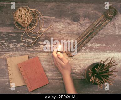 Femme main allume un bâton d'encens d'un support de Bouddha sur une surface en bois naturel vintage avec des livres, la ficelle de chanvre et de nombreux parfums aromatiques odorant s. Banque D'Images