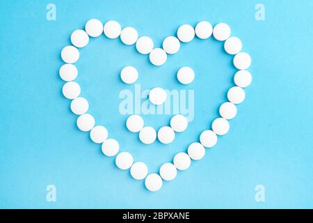 Sourire en forme de coeur smiley fait de pilules médicales blanches sur un fond de papier bleu. Concept de santé et de soins Banque D'Images