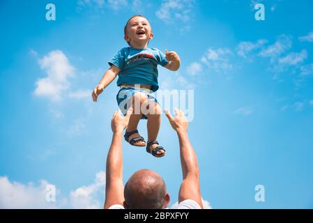 Père joue avec son fils et le lance pour voler dans le ciel bleu par un jour ensoleillé. Banque D'Images