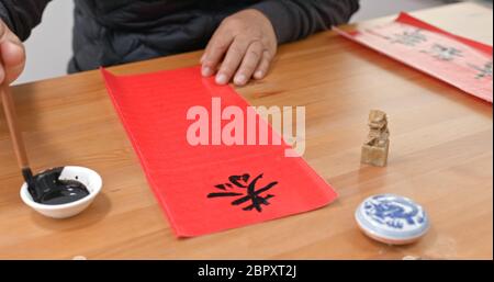 L'homme écrit la calligraphie chinoise pour la nouvelle année lunaire, les mots signifient vous souhaitent une année prospère Banque D'Images