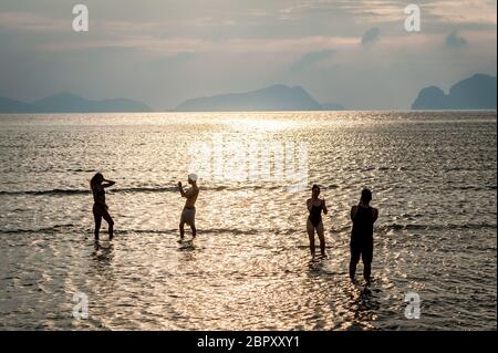 Les couples se sont enroulés dans l'eau pour admirer et photographier le coucher du soleil à Las Cabanas Beach, El Nido, Palawan, Philippines. Banque D'Images