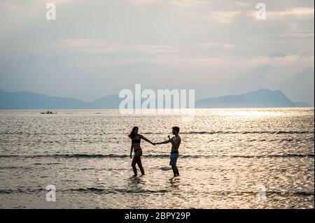 Les couples se sont enroulés dans l'eau pour admirer et photographier le coucher du soleil à Las Cabanas Beach, El Nido, Palawan, Philippines. Banque D'Images