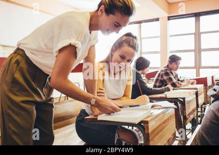 Une femme heureuse aide à l'adolescent en classe. Professeur de sexe féminin aidant une jeune fille étudiante pendant une classe au secondaire. Banque D'Images