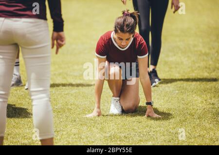 Fille en course à pied position de départ sur le terrain avec enseignant et les étudiants debout autour. Élèves en classe sportive dans le terrain scolaire. Banque D'Images