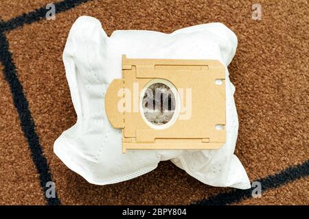 Vue de dessus du sac d'aspirateur usagé plein de poussière et de poils d'animaux sur fond de tapis marron Banque D'Images