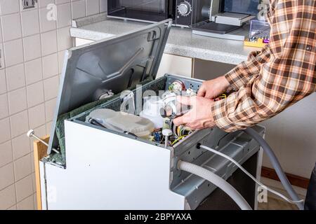 Les personnes en emploi de technicien. Technicien de réparation de l'appareil ou l'homme travaille sur lave-vaisselle cassée dans un kittchen. Ouvrier est en train de changer l'élément de chauffage. Banque D'Images