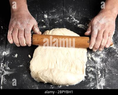 Chef dans une tunique noire roule une pâte pour une pizza ronde, vue du dessus Banque D'Images