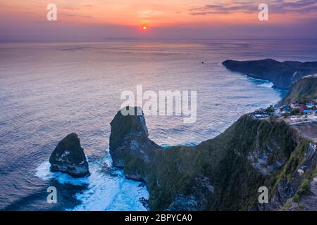 Vue aérienne montrant un magnifique coucher de soleil tropical sur de imposantes falaises et vagues de l'océan (Kelingking, Nusa Penida, Indonésie) Banque D'Images