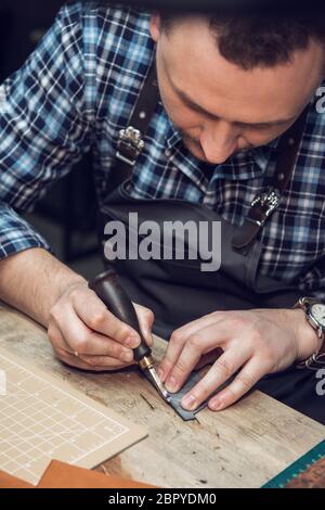 Travail avec le cuir homme lors d'un atelier textile. Concept de la production artisanale à la main des articles en cuir. Banque D'Images