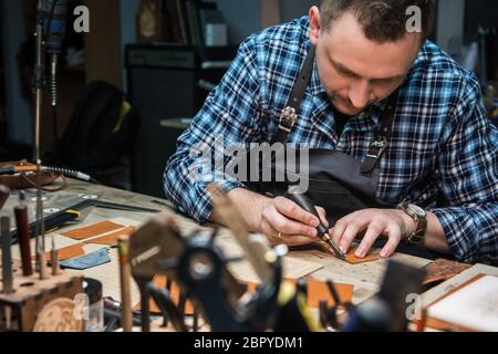 Travail avec le cuir homme lors d'un atelier textile. Concept de la production artisanale à la main des articles en cuir. Banque D'Images