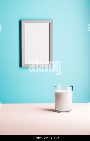 Un verre de lait sur une table. Un cadre en bois vide sur le mur pour une utilisation avec votre propre image ou message. Couleurs pastel. Banque D'Images