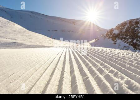 Lignes droites et rapprochées de pistes de ski fraîchement préparées, avec un soleil éclatant et un fond bleu clair. Montagne enneigée Banque D'Images