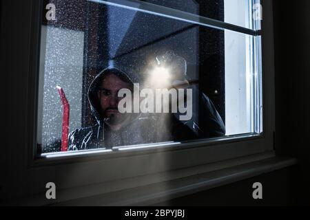 Burglar With Crowbar et lampe à Windows dans une maison Banque D'Images