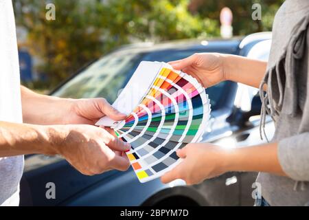Close-up of Man Showing échantillons de couleur à Woman standing in front of Car Banque D'Images