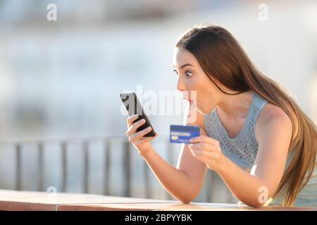 Surpris de l'acheteur en ligne holding cell phone payer achat dans un balcon Banque D'Images