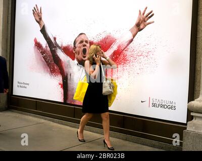 Une femme qui marche devant une affiche de Wayne Rooney parlant dans son téléphone portable bras levés en célébration. Banque D'Images