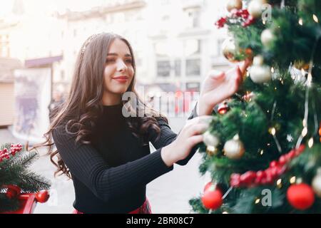 Fille souriante avec un boule d'arbre de Noël pour le a une bonne humeur de noël. Portrait d'une belle fille avec un jouet de Noël dans ses mains près d'un sapin Banque D'Images