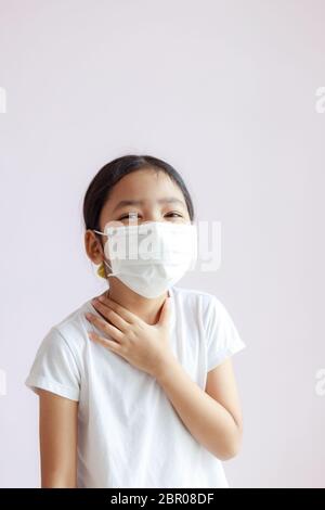 Portrait d'une petite fille asiatique touchant son cou avec un mal de gorge. L'enfant porte un masque sanitaire. L'épidémie de grippe, de coronavirus ou de COVID-19 Banque D'Images