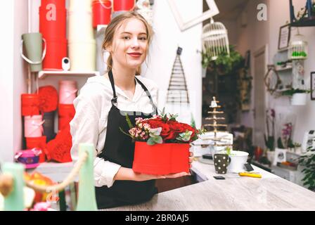 Jeune femme fleuriste en tablier noir tient dans les mains boîte à chapeau avec des fleurs Banque D'Images