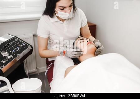 Traitement par microcourant. Le cosmologiste fait un massage stimulant du visage avec des gants électriques. Massage du drainage lymphatique Banque D'Images