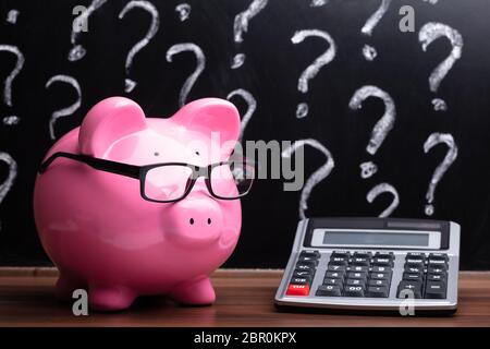 Close-up of a Pink Piggybank avec lunettes et calculateur sur un bureau en bois Banque D'Images