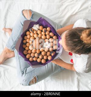 Jeune femme assise sur le lit avec noix de coco et de bouquet dans l'alimentation des mains. Vue de dessus sur les jeunes femme hipster en jean déchiré au genou avec une rare Banque D'Images