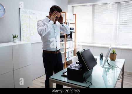 Irrité jeune Businessman Looking At Imprimante dans Office Banque D'Images