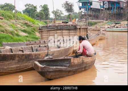 Une femme cambodgienne sur un bateau sur le fleuve avec des maisons sur pilotis en arrière-plan à Kampong Phluk, province de Siem Reap, centre-nord du Cambodge. Banque D'Images