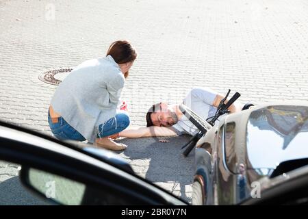 Young Woman Lying On cycliste homme inconscient après un accident de voiture près de la rue Banque D'Images