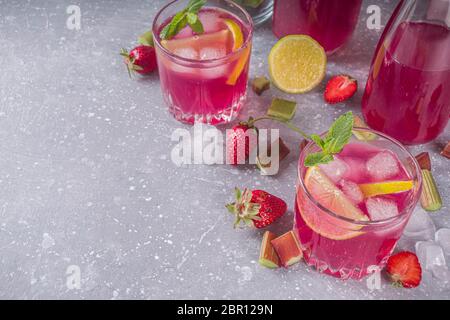 Rhubarbe maison et cocktail d'alcool aux fraises. Liqueur ou gin de rhubarbe, sur fond gris avec rhubarbe fraîche, fraises, citron, menthe Banque D'Images