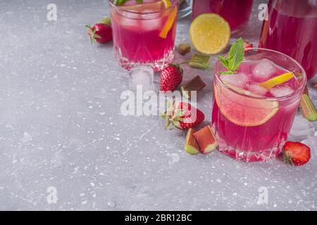 Rhubarbe maison et cocktail d'alcool aux fraises. Liqueur ou gin de rhubarbe, sur fond gris avec rhubarbe fraîche, fraises, citron, menthe Banque D'Images