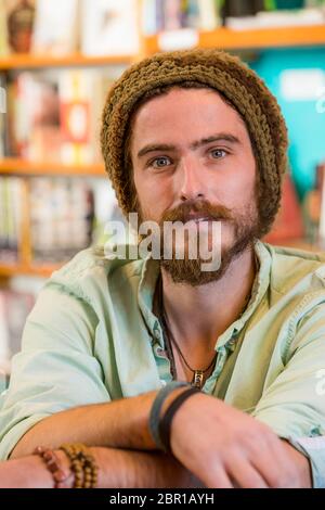 Beau jeune homme avec bonnet en tricot dans un magasin de livres ou une bibliothèque Banque D'Images